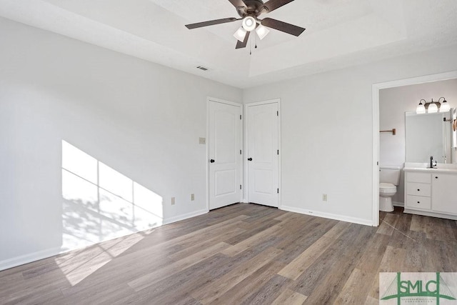 unfurnished bedroom with ensuite bath, a raised ceiling, ceiling fan, sink, and light hardwood / wood-style flooring