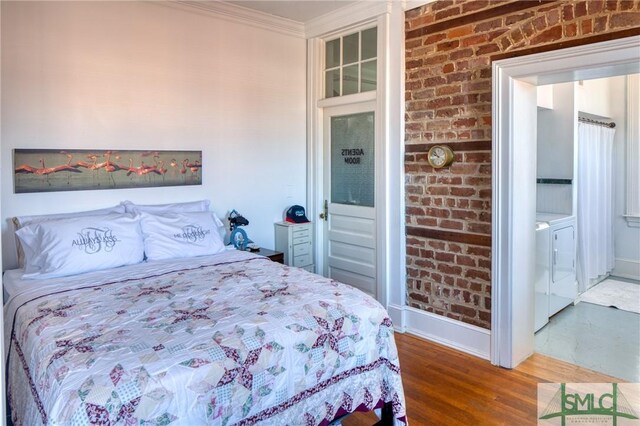 bedroom with washer and clothes dryer, hardwood / wood-style floors, brick wall, and ornamental molding