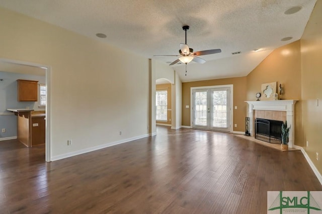 unfurnished living room featuring dark hardwood / wood-style flooring, lofted ceiling, a textured ceiling, and a tiled fireplace