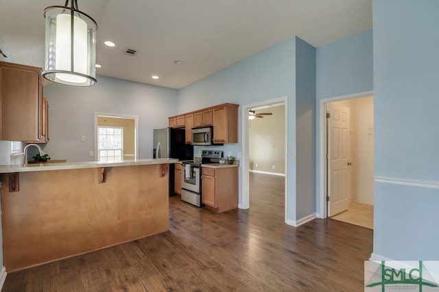 kitchen featuring a kitchen bar, appliances with stainless steel finishes, kitchen peninsula, decorative light fixtures, and dark hardwood / wood-style floors