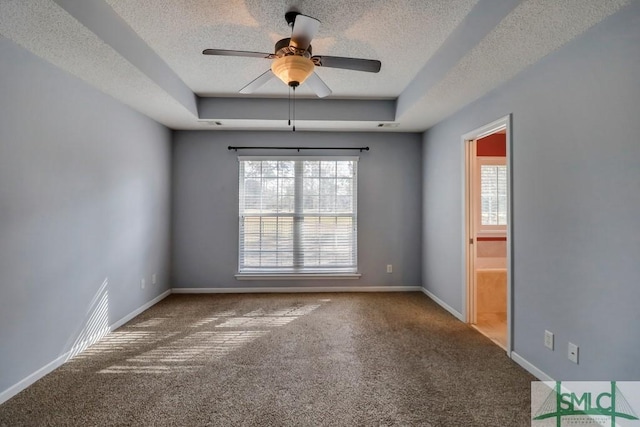 empty room with a raised ceiling, ceiling fan, carpet, and a textured ceiling