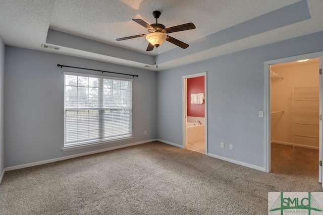 unfurnished bedroom with a raised ceiling, a walk in closet, ensuite bathroom, and a closet