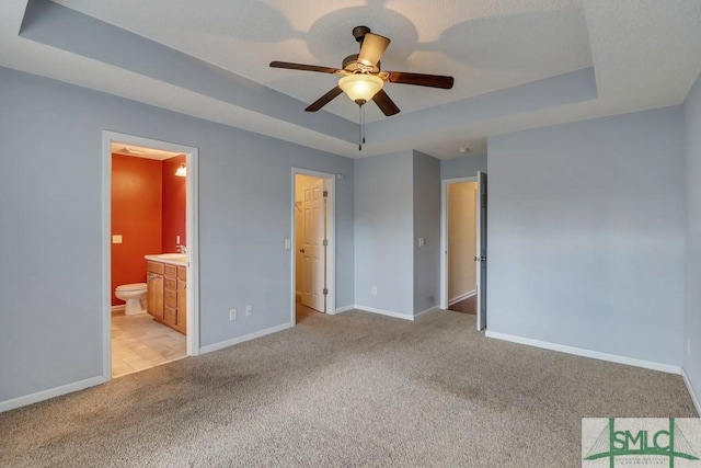 unfurnished bedroom with light carpet, ensuite bath, a raised ceiling, ceiling fan, and a closet