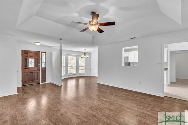 unfurnished living room with ceiling fan with notable chandelier, a raised ceiling, and dark wood-type flooring