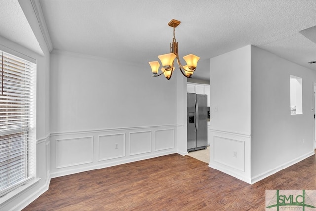 empty room with a textured ceiling, a notable chandelier, ornamental molding, and dark wood-type flooring