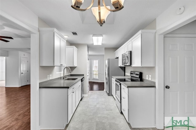 kitchen featuring appliances with stainless steel finishes, light wood-type flooring, ceiling fan with notable chandelier, sink, and white cabinetry