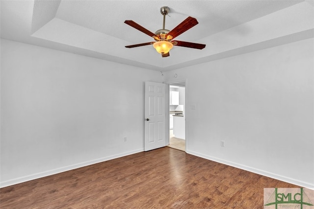 unfurnished room with wood-type flooring, a tray ceiling, and ceiling fan