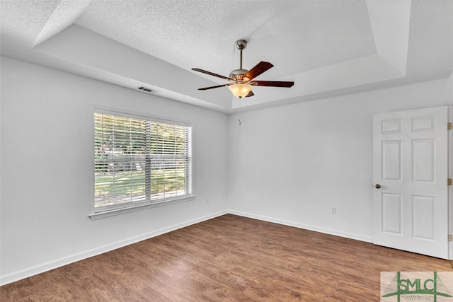 empty room with a raised ceiling, ceiling fan, dark wood-type flooring, and a textured ceiling