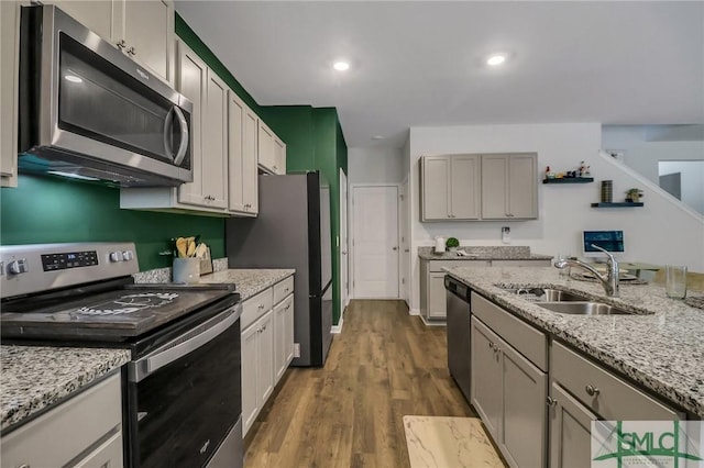 kitchen with gray cabinetry, sink, light stone counters, hardwood / wood-style floors, and appliances with stainless steel finishes