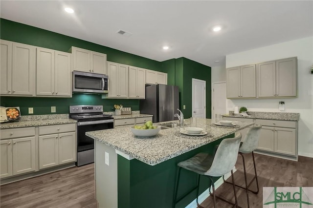 kitchen with light stone countertops, stainless steel appliances, sink, a center island with sink, and dark hardwood / wood-style floors