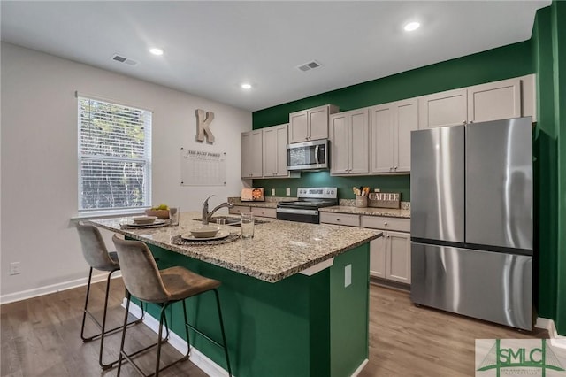 kitchen featuring hardwood / wood-style floors, white cabinets, sink, an island with sink, and appliances with stainless steel finishes