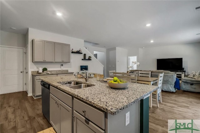 kitchen with dark wood-type flooring, a center island with sink, sink, stainless steel dishwasher, and gray cabinets