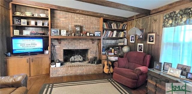 living room with wood-type flooring, a brick fireplace, beam ceiling, and wood walls