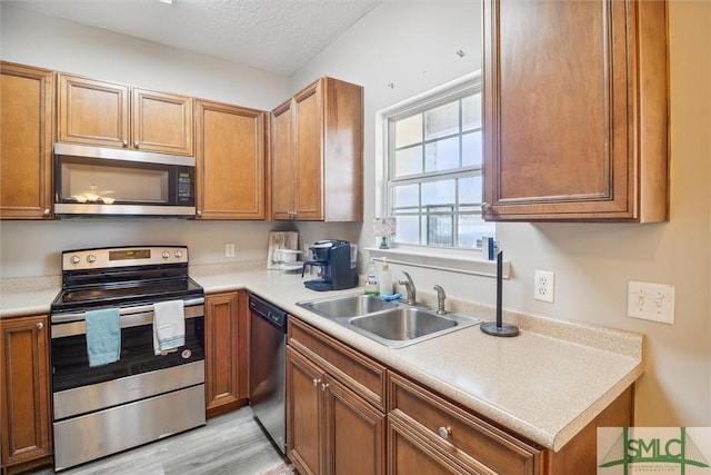 kitchen with a textured ceiling, appliances with stainless steel finishes, light hardwood / wood-style flooring, and sink