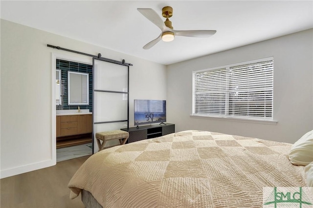 bedroom with hardwood / wood-style flooring, ceiling fan, a barn door, and ensuite bath