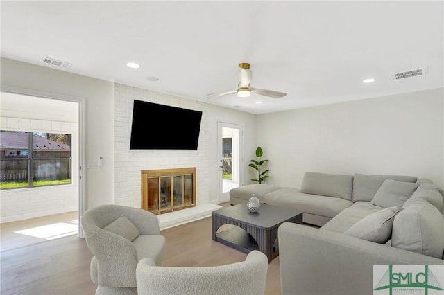 living room featuring a brick fireplace, ceiling fan, and light wood-type flooring