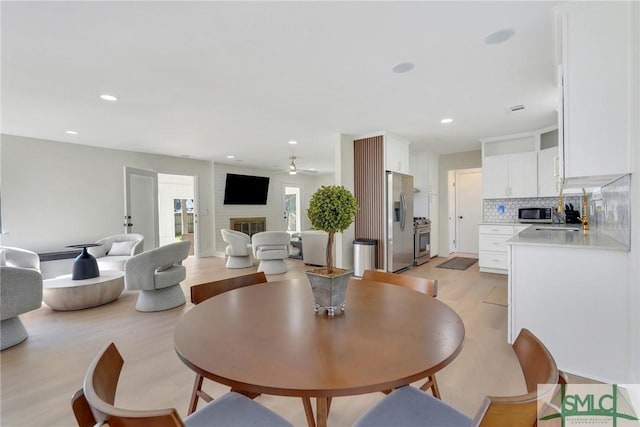 dining room with a fireplace, light hardwood / wood-style floors, and ceiling fan