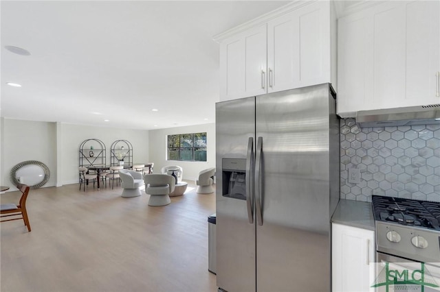 kitchen with appliances with stainless steel finishes, backsplash, hardwood / wood-style flooring, white cabinetry, and range hood