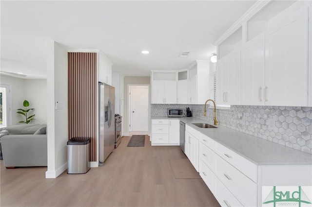 kitchen with decorative backsplash, appliances with stainless steel finishes, light wood-type flooring, sink, and white cabinets