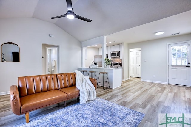 living room with ceiling fan, vaulted ceiling, light hardwood / wood-style floors, and sink