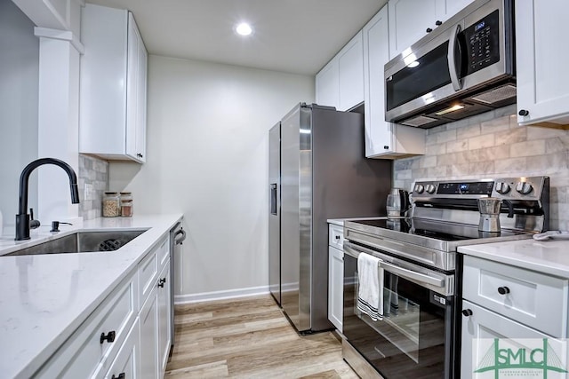 kitchen featuring stainless steel appliances, sink, white cabinetry, light stone counters, and light hardwood / wood-style flooring