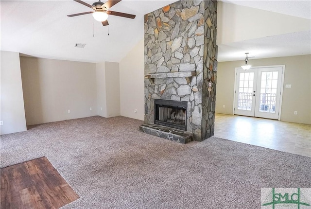 unfurnished living room featuring ceiling fan, french doors, a stone fireplace, vaulted ceiling, and light carpet