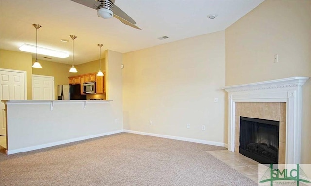 unfurnished living room featuring ceiling fan, light carpet, and a tile fireplace