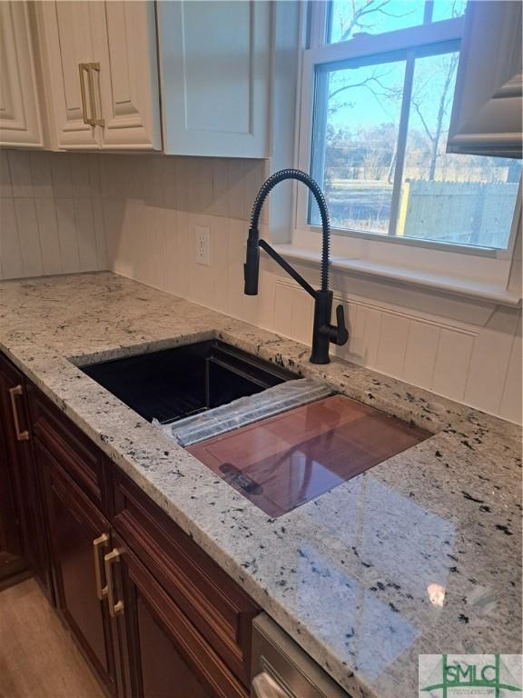 kitchen with white cabinetry, light stone countertops, sink, dark brown cabinets, and light wood-type flooring