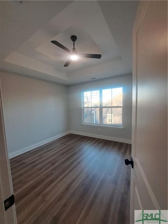 empty room featuring ceiling fan, a raised ceiling, and dark wood-type flooring