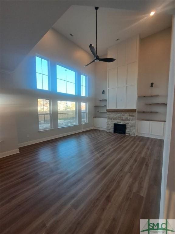 unfurnished living room with a stone fireplace, ceiling fan, dark hardwood / wood-style flooring, and a high ceiling