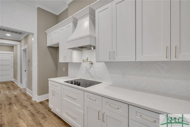 kitchen with premium range hood, white cabinetry, black electric stovetop, and crown molding