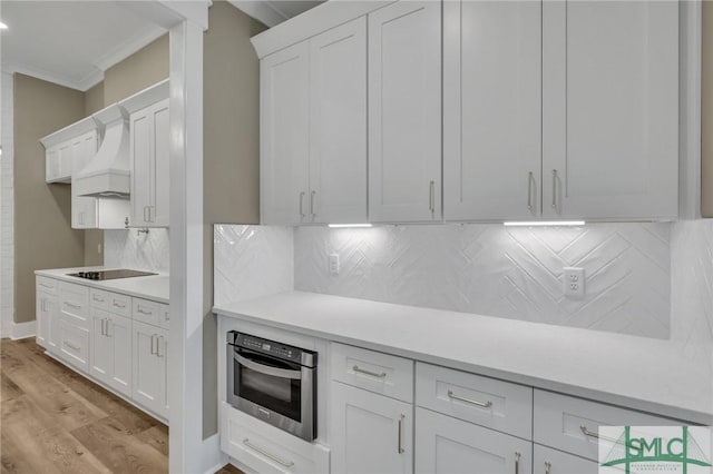 kitchen featuring white cabinetry, stainless steel oven, tasteful backsplash, light hardwood / wood-style flooring, and crown molding