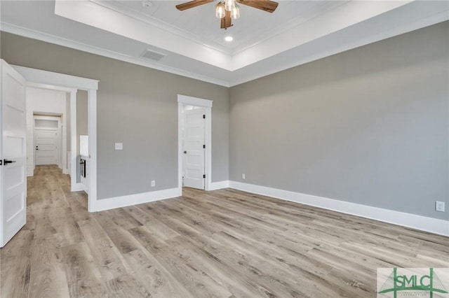 unfurnished bedroom with ceiling fan, a raised ceiling, light wood-type flooring, and crown molding