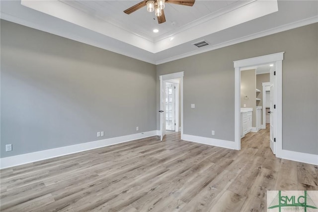 unfurnished bedroom with light wood-type flooring, ensuite bath, a raised ceiling, ceiling fan, and crown molding