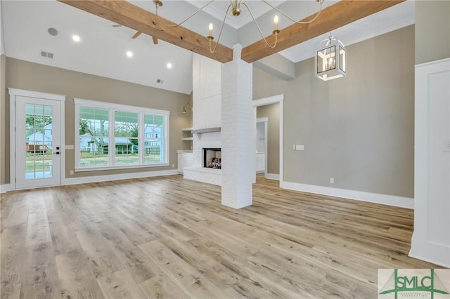 unfurnished living room featuring a high ceiling, light hardwood / wood-style floors, a brick fireplace, and a healthy amount of sunlight