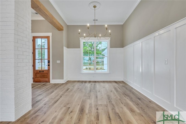 unfurnished dining area featuring light wood-type flooring, an inviting chandelier, a wealth of natural light, and ornamental molding