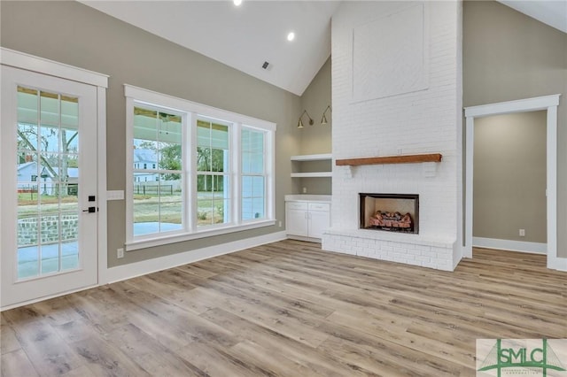 unfurnished living room with light hardwood / wood-style floors, a healthy amount of sunlight, built in features, and a brick fireplace