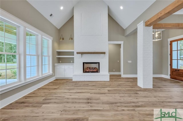 unfurnished living room featuring plenty of natural light, built in shelves, a fireplace, and light hardwood / wood-style flooring