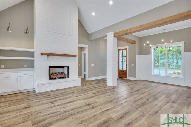 unfurnished living room with light wood-type flooring, an inviting chandelier, a brick fireplace, and high vaulted ceiling