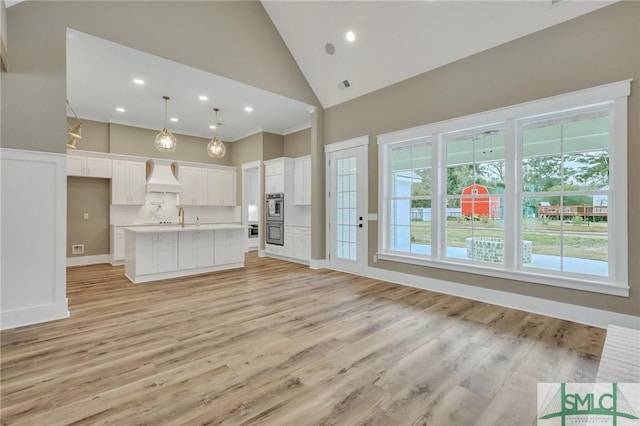 unfurnished living room featuring light hardwood / wood-style flooring, high vaulted ceiling, plenty of natural light, and sink