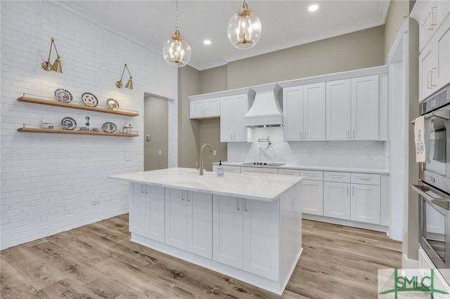 kitchen featuring premium range hood, light stone counters, pendant lighting, white cabinetry, and oven