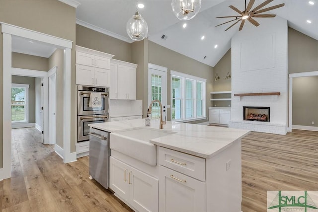 kitchen featuring a kitchen island with sink, sink, appliances with stainless steel finishes, decorative light fixtures, and white cabinetry