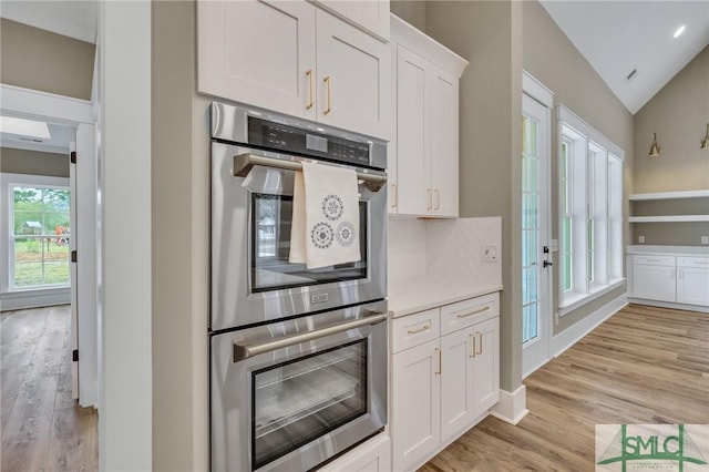 kitchen featuring backsplash, vaulted ceiling, double oven, light hardwood / wood-style floors, and white cabinetry