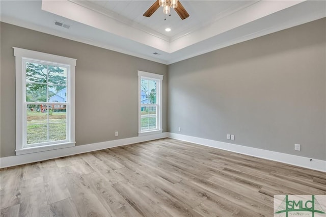 empty room with a tray ceiling, ceiling fan, light hardwood / wood-style flooring, and crown molding