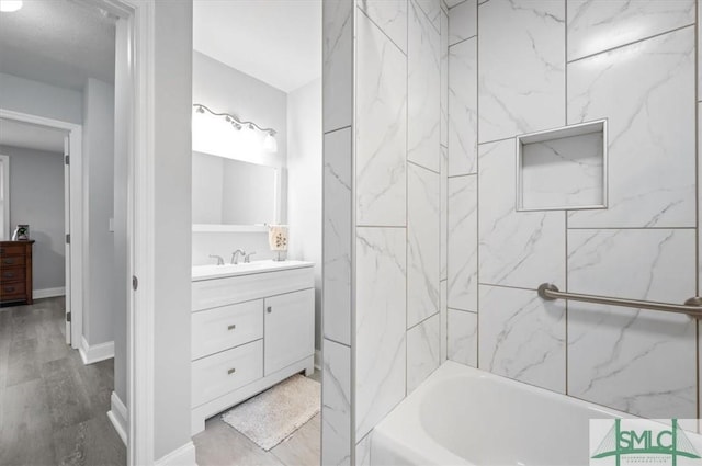 bathroom featuring washtub / shower combination, baseboards, wood finished floors, and vanity