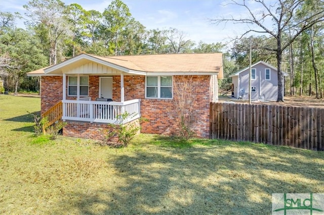 view of front of house with covered porch, brick siding, a front lawn, and fence