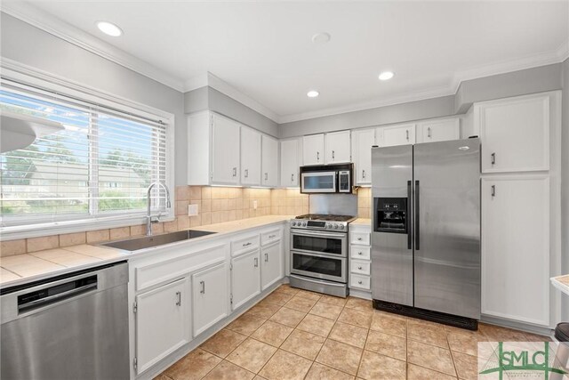 kitchen with white cabinets, appliances with stainless steel finishes, light tile patterned flooring, and sink