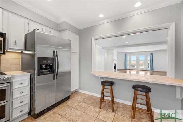 kitchen featuring a kitchen bar, tasteful backsplash, stainless steel appliances, tile countertops, and white cabinets