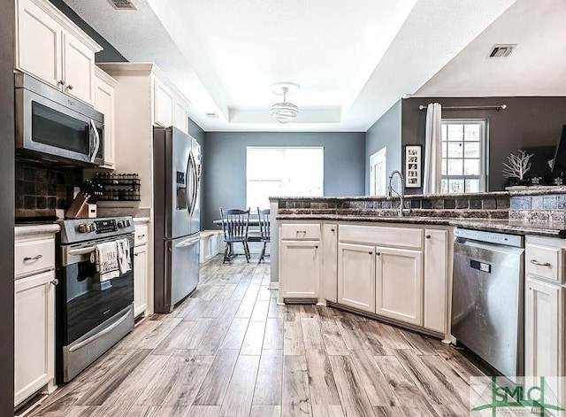 kitchen featuring sink, a raised ceiling, dark stone counters, white cabinets, and appliances with stainless steel finishes