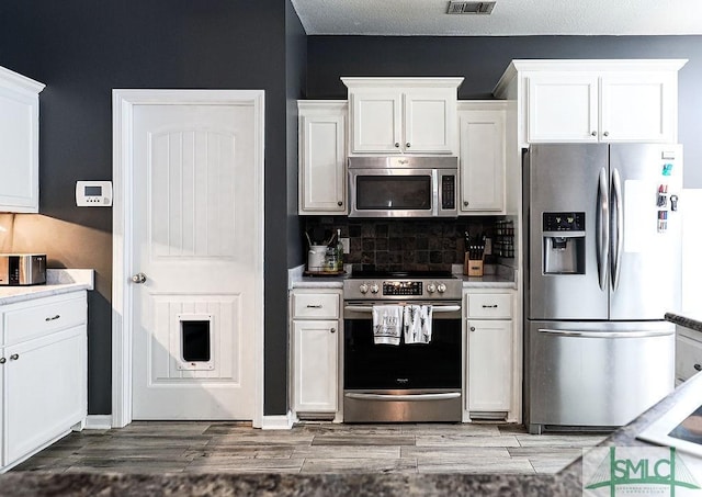 kitchen featuring tasteful backsplash, a textured ceiling, stainless steel appliances, hardwood / wood-style floors, and white cabinetry